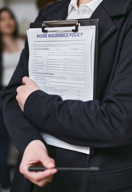 A woman with long blonde hair wearing a dark green T-shirt is inside a room, holding a clipboard and a black marker, appearing to check or record details related to the house removal process. Behind h